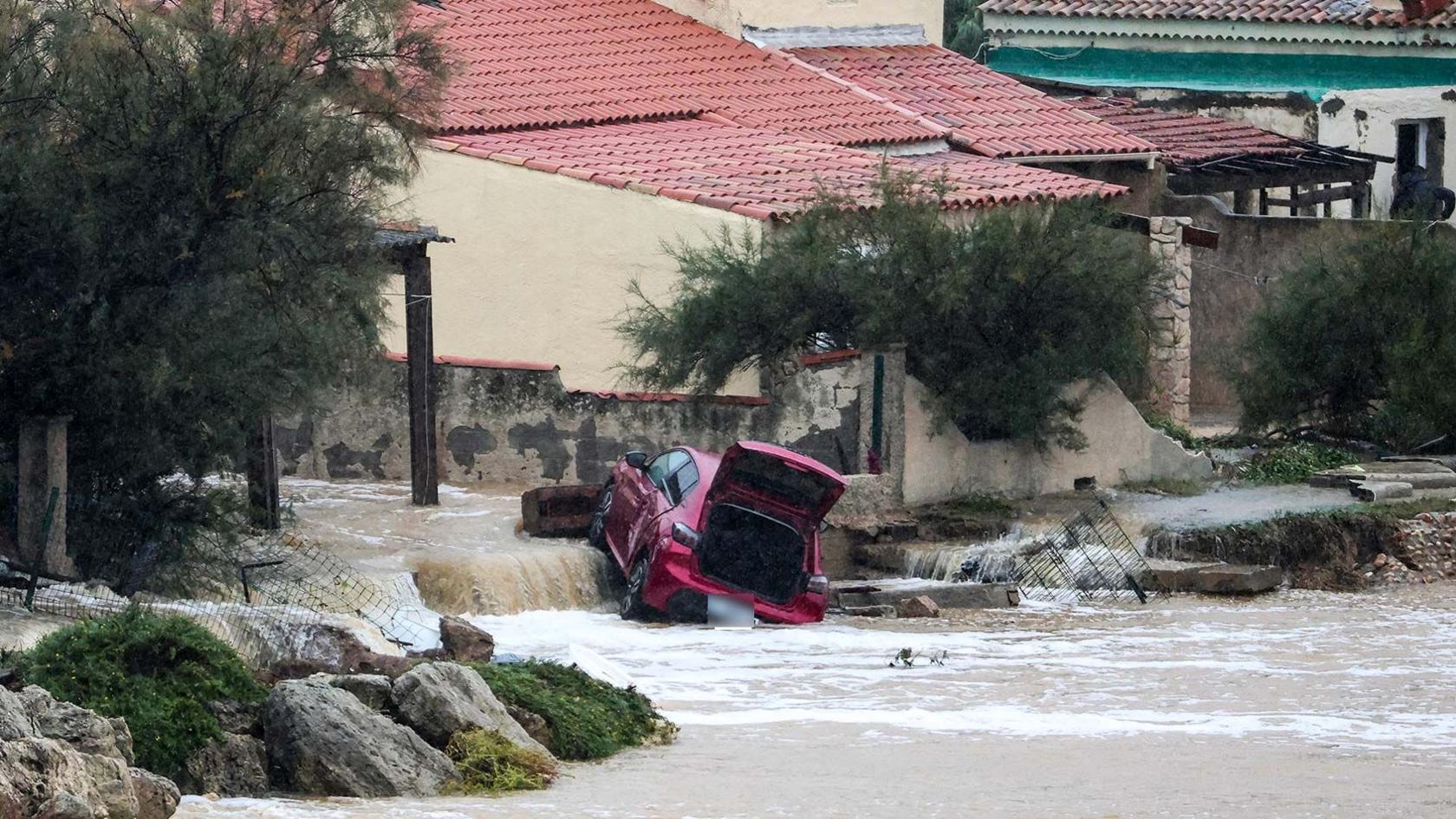 A damaged red car, lying at an angle with its boot open, in a flooded area