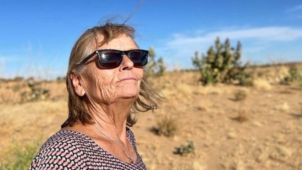 Eva Gretzmacher wearing sunglasses and a necklace, looking out over a desert landscape
