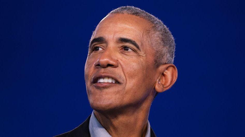 Barack Obama standing on a stage and smiling during his Glasgow speech